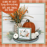 Decorative tray with pumpkins, flowers, and a framed picture on a plaid background