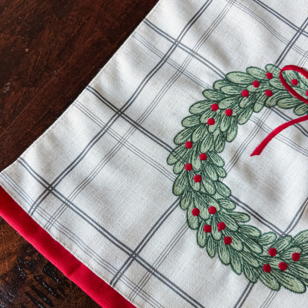 Plaid fabric with a embroidered green wreath and red accents on a wooden surface