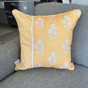 Yellow throw pillow with white floral embroidery and patterned fabric panel, displayed on a gray couch.
